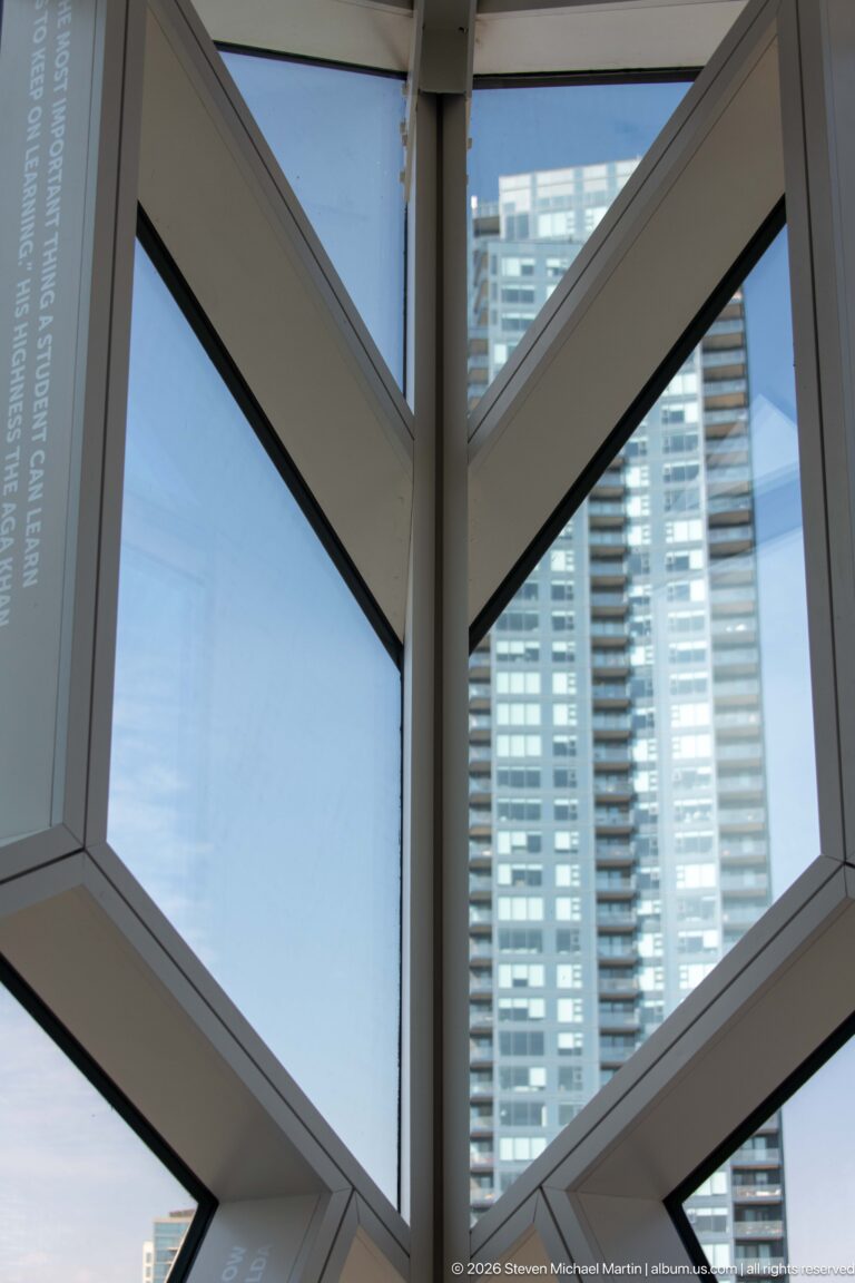 Angular white window framing inside Calgary Central Library with a residential tower visible beyond.