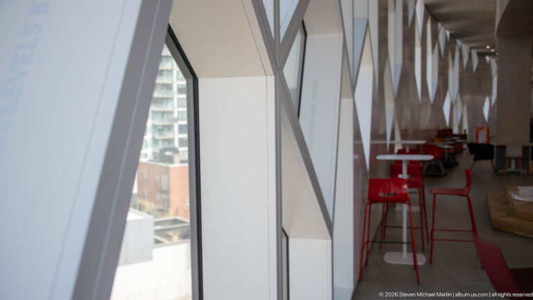 Red chairs and small tables beside tall angular windows inside Calgary Central Library.