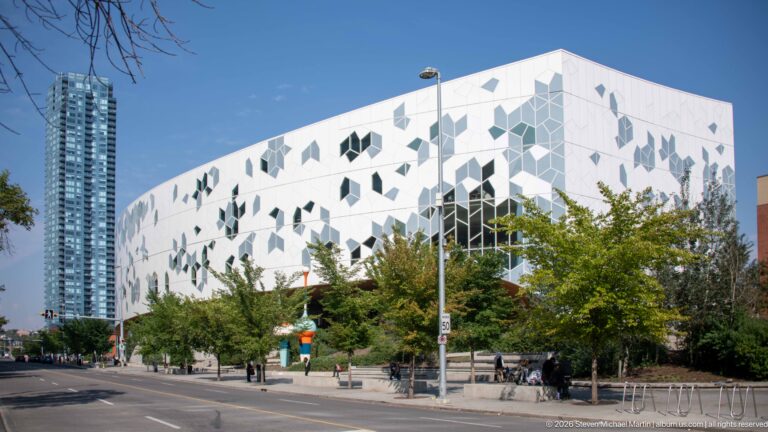 Calgary Central Library’s white geometric façade and irregular windows viewed from a tree-lined city street.