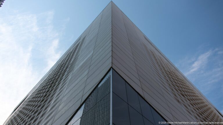 Sharp corner of Calgary Central Library rising into blue sky, with pale patterned cladding and dark glazing.