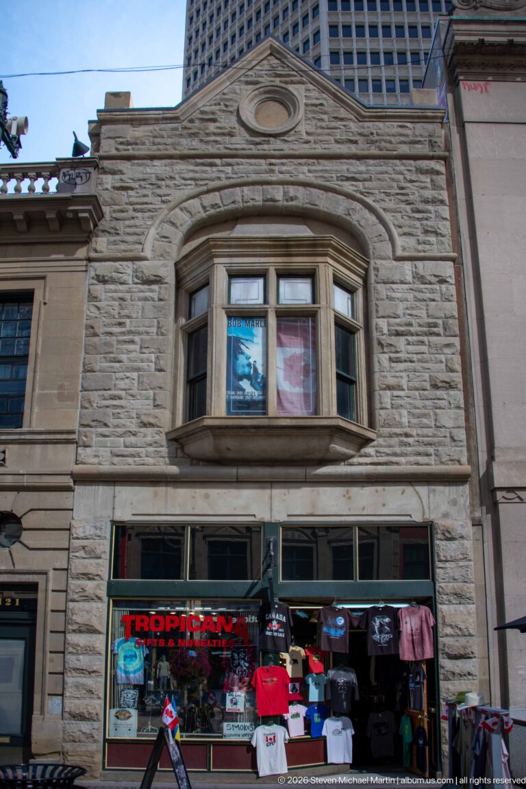 Rusticated stone historic façade with bay window above the colorful Tropicana souvenir storefront in Calgary.