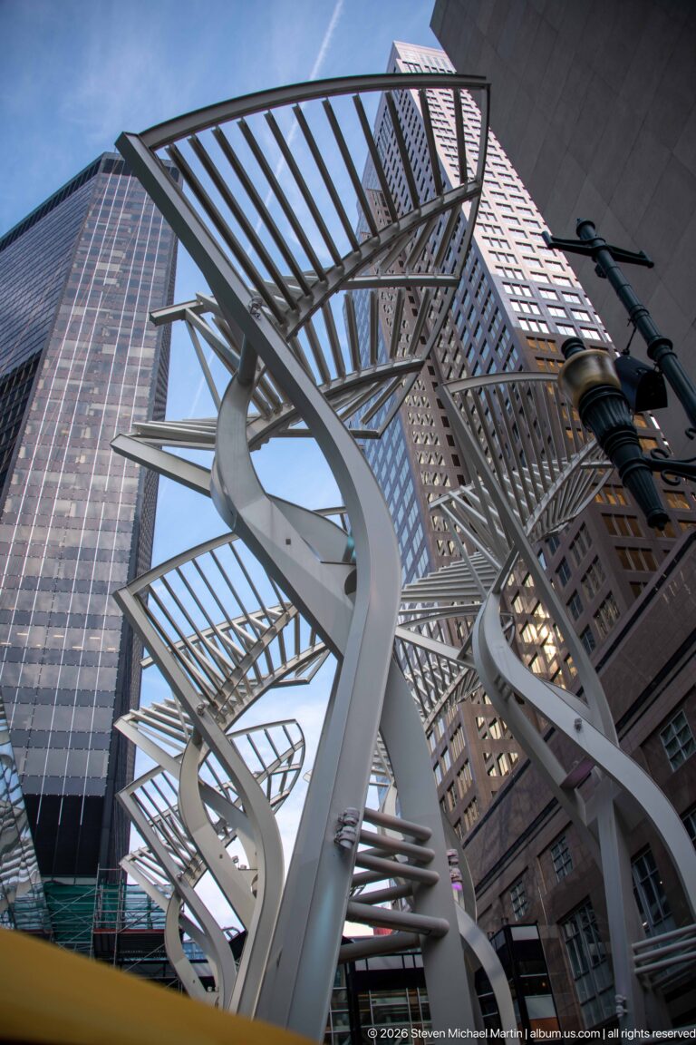 Several white Galleria Trees with slotted metal canopies rising between office towers along Stephen Avenue in Calgary.