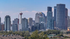 Calgary Tower amid dense downtown residential and office towers, viewed above trees and low buildings.