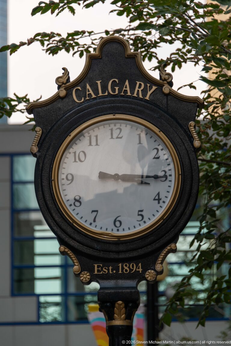 Decorative black and gold street clock labeled Calgary and Est. 1894, with a modern building behind.