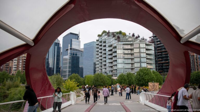 Large red Peace Bridge arch framing pedestrians, trees, and modern residential towers beyond the bridge.