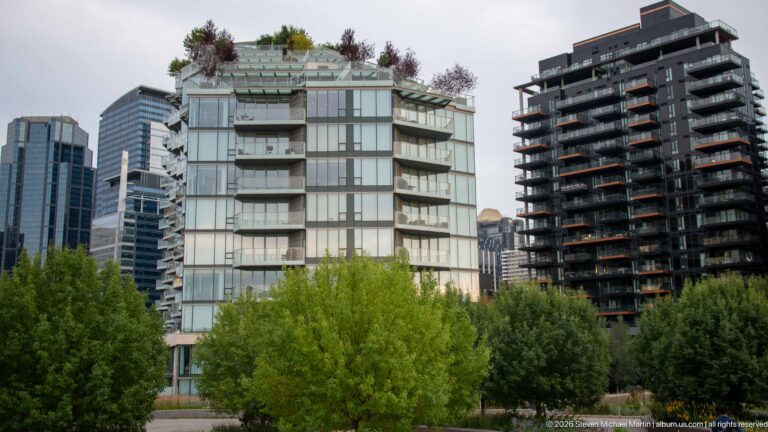 Modern glass-fronted residential towers rising behind leafy trees in Calgary.
