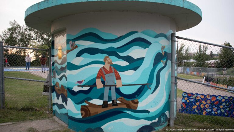 Cylindrical park structure painted with a figure, stylized blue waves, and colorful decorative motifs.