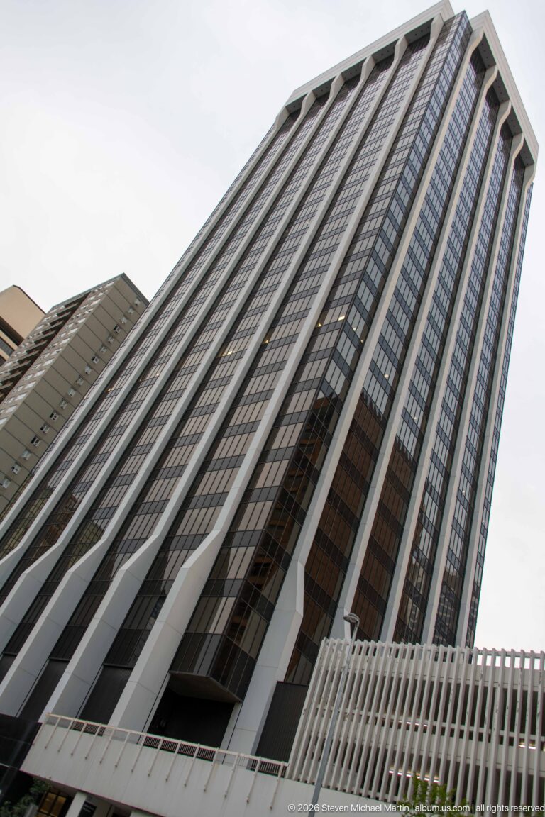 Low-angle view up a tall Calgary office tower with pale vertical ribs and dark window bands.