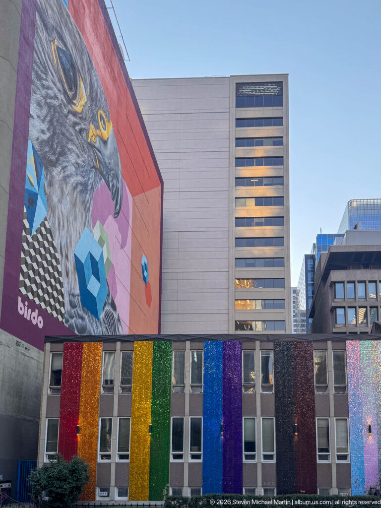 Large eagle mural above a building façade covered with vertical red, orange, yellow, green, blue, purple, and shimmering panels.