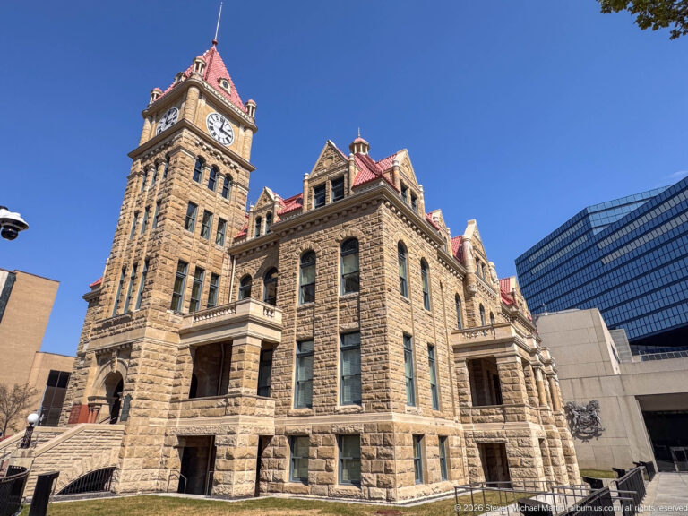 Historic sandstone Calgary City Hall with clock tower and red roofs, backed by modern downtown buildings.