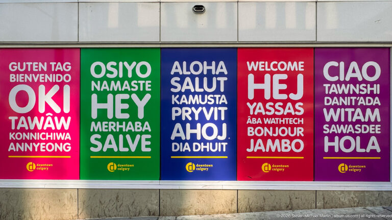 Five colorful Downtown Calgary posters displaying welcome greetings in many languages, including Oki, Hey, Aloha, Hej, Ciao, and Hola.