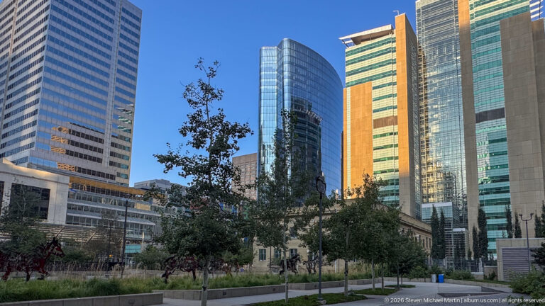 Landscaped downtown Calgary green space surrounded by striped, curved glass, and reflective office towers.