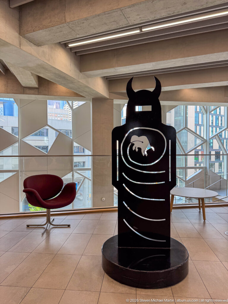 Black upright sculpture with horn-like top, white concentric lines, and animal silhouette inside Calgary Central Library.