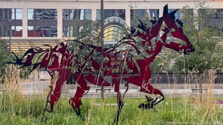 Close view of overlapping burgundy and dark openwork metal horse sculptures standing among tall grasses.