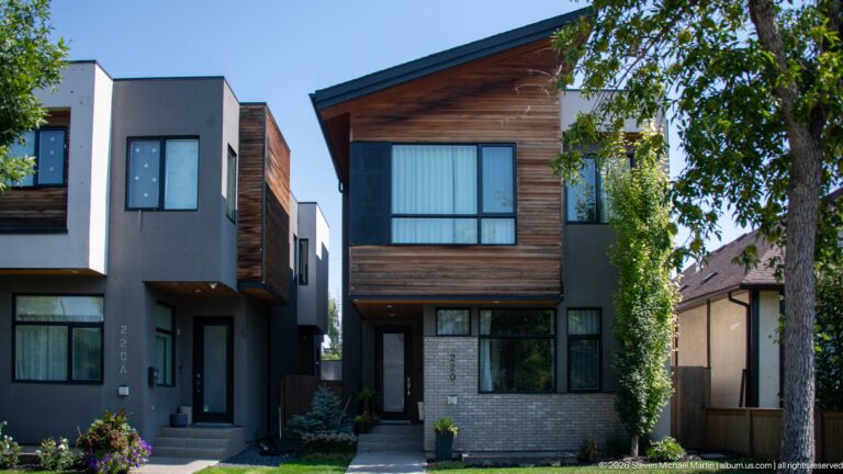 Two narrow modern Calgary infill houses with wood cladding, gray walls, pale brick, and large black-framed windows.