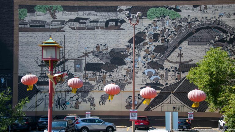 Large historical Chinese street-scene mural in Calgary Chinatown with red lanterns hanging across the foreground.