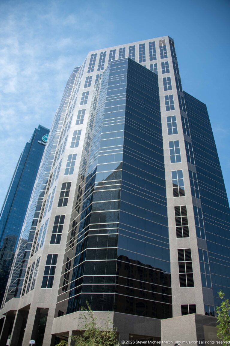 Modern Calgary office tower with black reflective glass and a pale rectangular grid wrapping its façade.