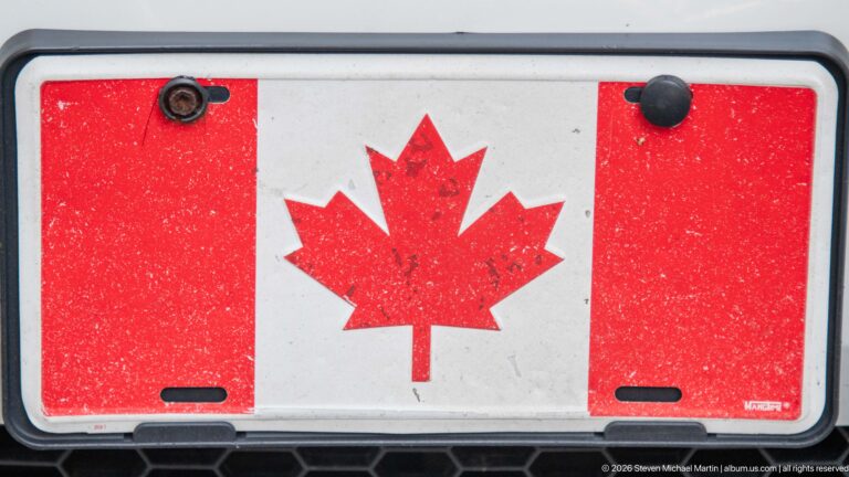 Weathered Canadian flag plate with red maple leaf mounted on a dark vehicle surface.
