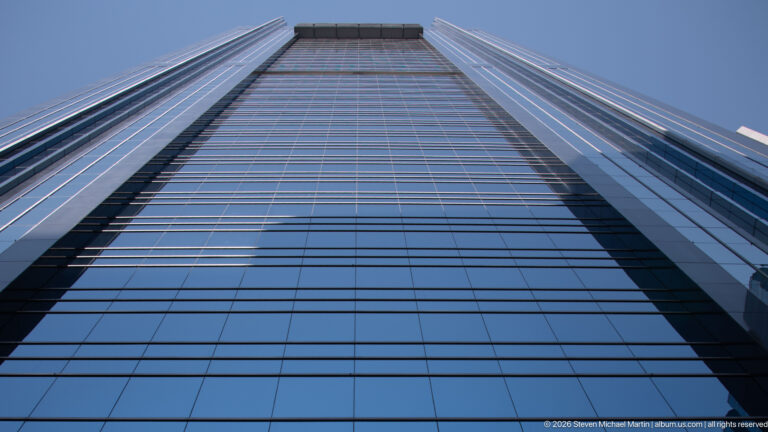 Extreme upward view of a reflective blue-glass Calgary skyscraper with gridded façade and projecting crown.
