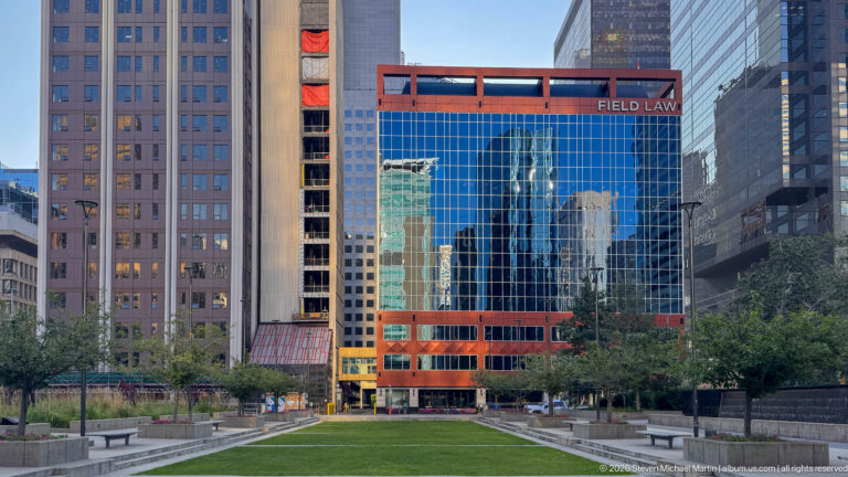 Field Law office building with reflective blue-glass façade and red framing beyond a landscaped downtown lawn.