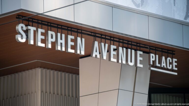 Large white Stephen Avenue Place lettering mounted beneath a wood-toned soffit on a modern building.