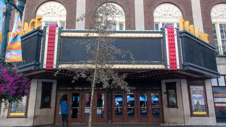 Palace Theatre entrance on Stephen Avenue with bulb-lined marquee, wooden doors, poster cases, and tall arched windows above.