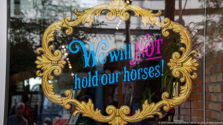Ornate gold scrollwork framing colorful window lettering that reads, We will NOT hold our horses!.