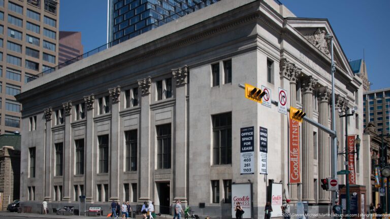 Oblique view along the Bank of Montreal’s long stone side façade with tall windows, pilasters, and pedestrians.