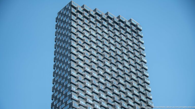 Upper stories of a modern Calgary residential tower with a dense grid of projecting balconies against blue sky.