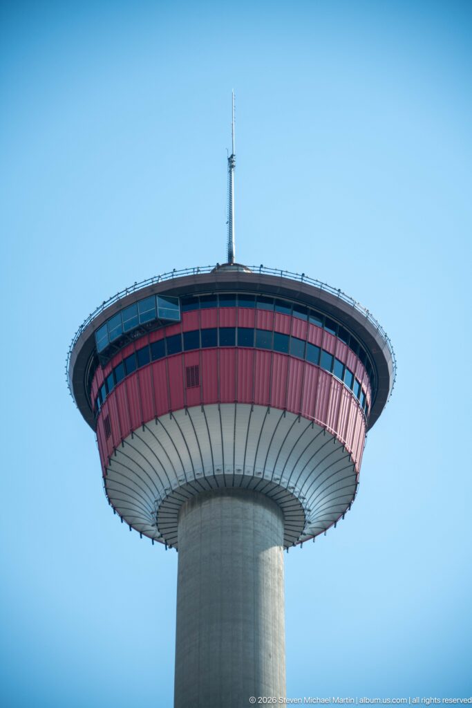 Close upward view of Calgary Tower’s red-glazed circular observation deck, concrete shaft, and rooftop antenna.