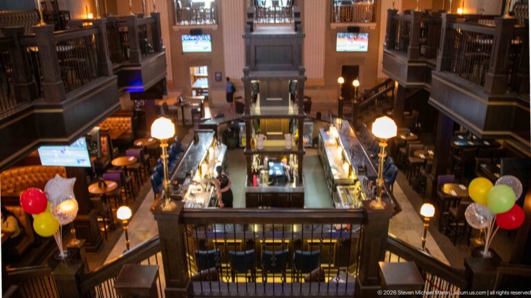 Elevated view over the Bank & Baron central bar, galleries, globe lamps, seating, and colorful balloons.