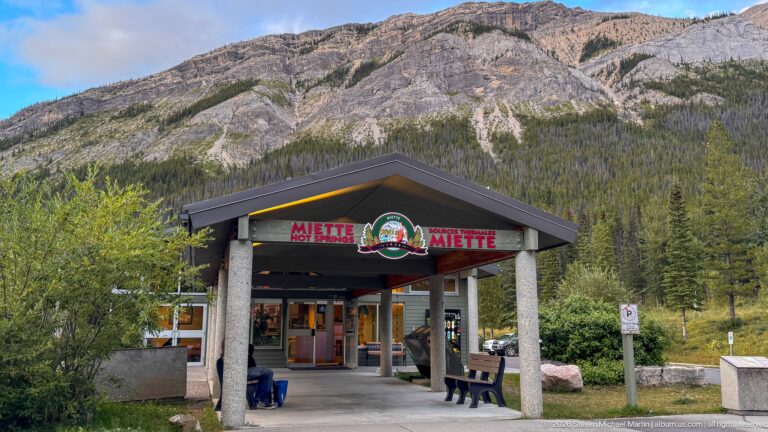 Front entrance canopy of Miette Hot Springs with bilingual signage and emblem below a broad rocky mountain slope.