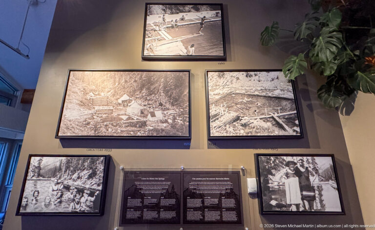 Wall display of framed black-and-white historic photographs showing earlier Miette Hot Springs buildings, pools, and visitors.