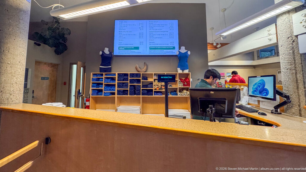 Service counter with computers, staff, open shelving, folded textiles, merchandise, and digital information boards.