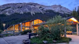 Miette Hot Springs building glowing at dusk beneath steep gray mountain cliffs and conifer forest.