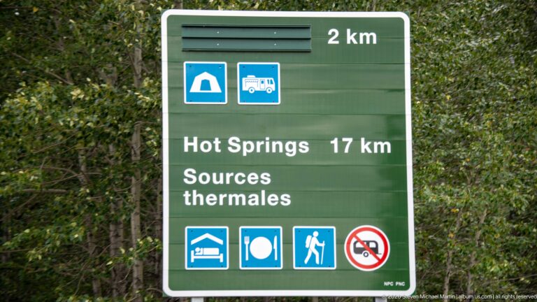 Green bilingual services sign reading Hot Springs 17 km and Sources thermales, with camping, lodging, food, and hiking icons.
