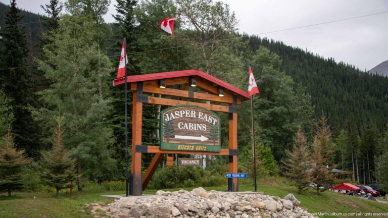 Timber sign reading Jasper East Cabins with Canadian flags and a forested mountain slope behind.