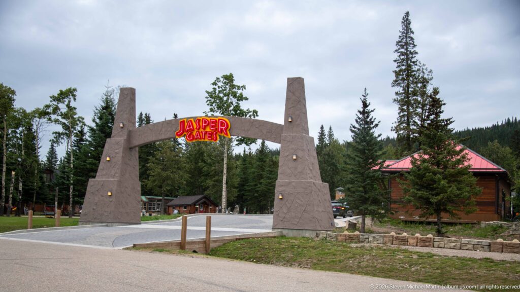 Stone-colored entrance arch reading Jasper Gates over a driveway, surrounded by conifers and rustic buildings.