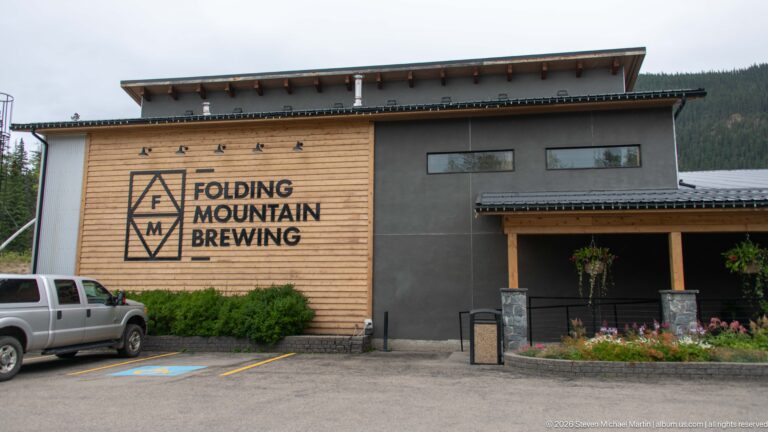 Folding Mountain Brewing building with wood siding, dark panels, large logo, covered entrance, and parked vehicles.