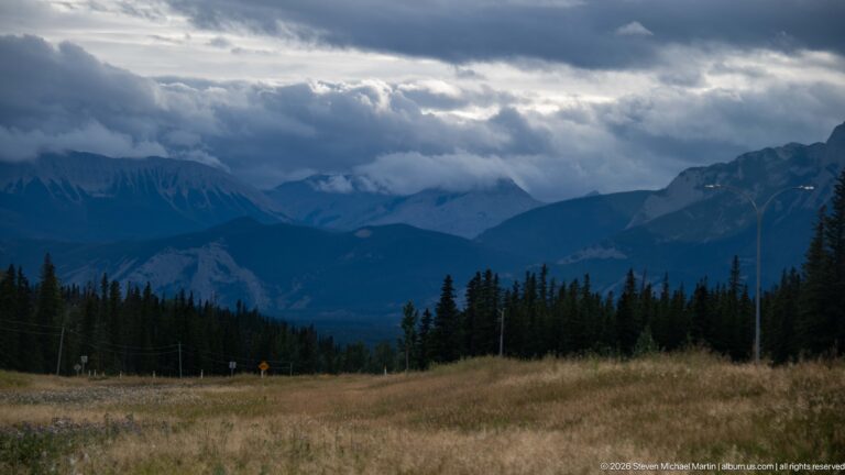 Dark storm clouds and low mist over layered mountain ridges and a forested valley in Jasper National Park.