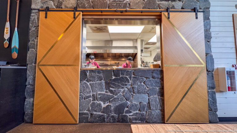 Open restaurant kitchen framed by dark stone and large sliding wooden doors, with stainless equipment and staff visible inside.