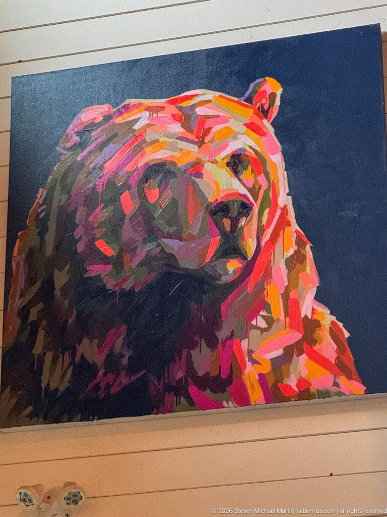 Large colorful painting of a bear head in red, orange, pink, purple, and dark tones against a deep blue background.