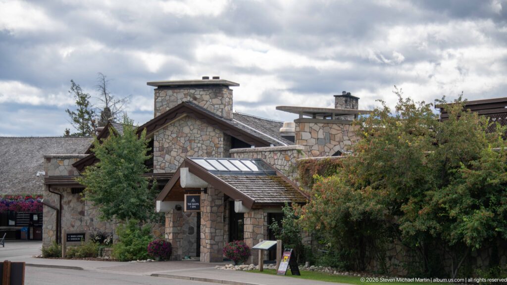 Layered stone lodge buildings with broad chimneys, pitched roofs, trees, and landscaped approach.