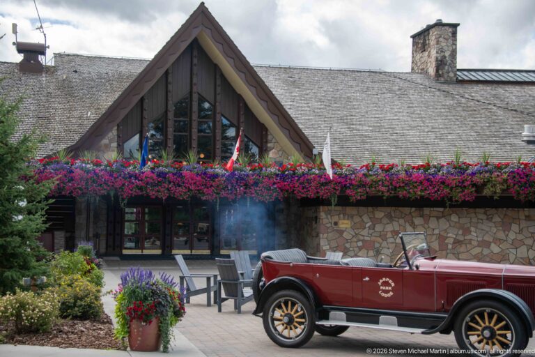 Burgundy Jasper Park Lodge touring car parked before a steep gabled entrance lined with flowers.