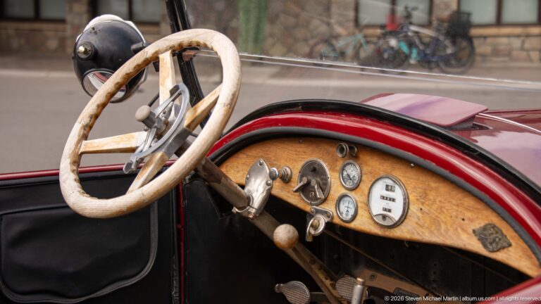Close view of pale steering wheel, wood dashboard, gauges, and controls inside a burgundy touring car.