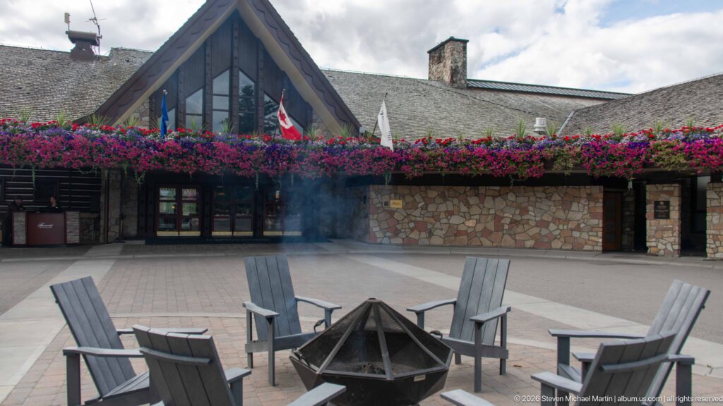 Gray chairs around a courtyard fire pit beneath a flower-lined stone-and-timber lodge façade.