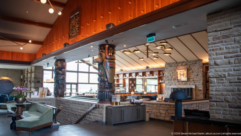 Large figuratively carved wooden columns rising among stone walls and lounge seating inside Jasper Park Lodge.