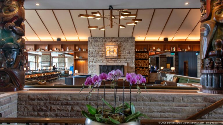 Pink orchids in front of a stone wall, fireplace, bar, and wood-paneled Jasper Park Lodge lounge.