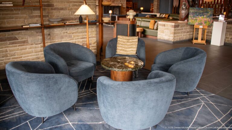 Four blue-gray lounge chairs arranged around a small round table beside a low stone wall.