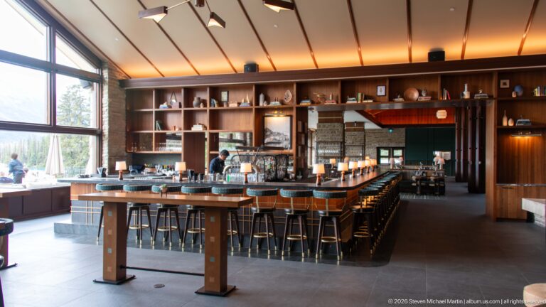 Long lodge bar with upholstered stools, wood shelving, table lamps, and stone architectural accents.
